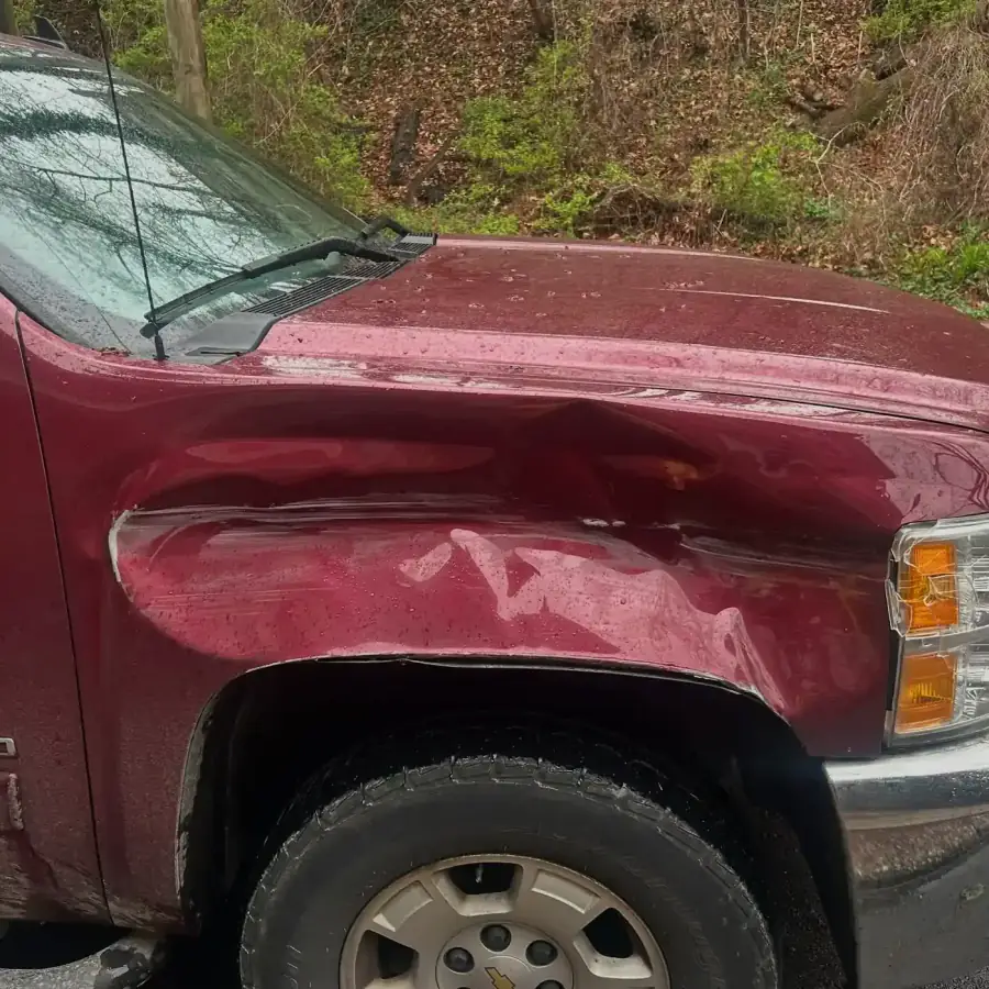 Maroon Chevy Silverado work truck with a dented front fender before repair
