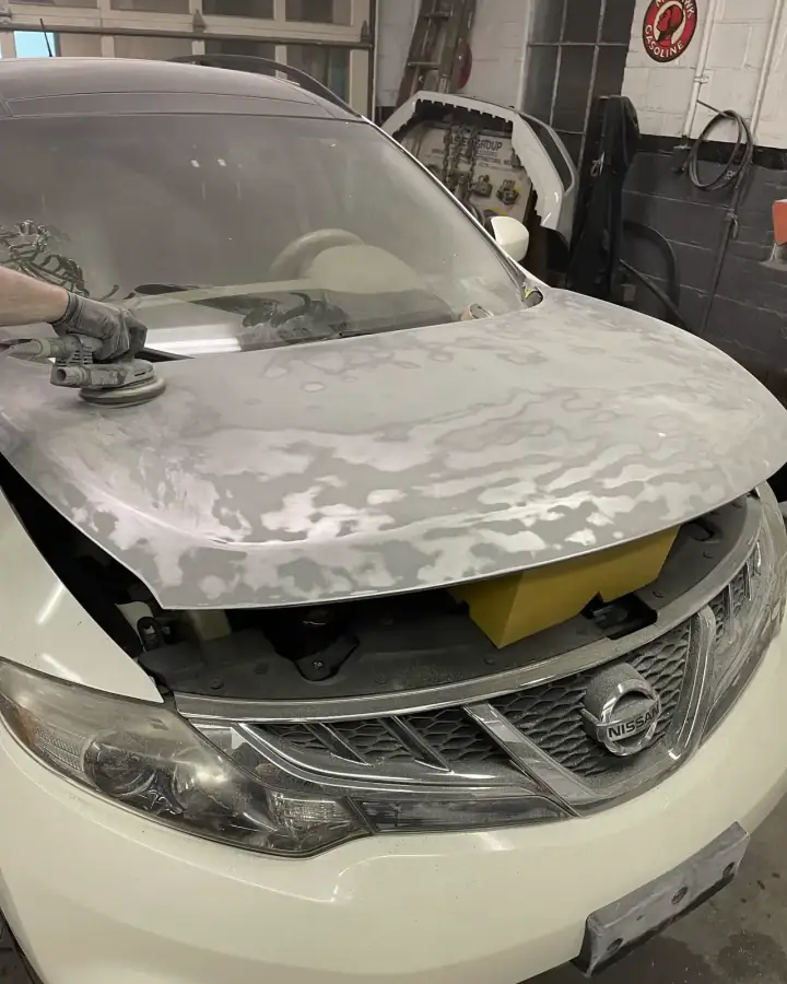 Technician sanding the peeling clear coat off a white Nissan Murano hood before repainting in Lansdowne, PA